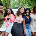 Group of five happy african american girls sitting on a car hood.