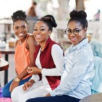 Three casual african american girls with colored shopping bags walking outdoor. Stylish black womans shopping.